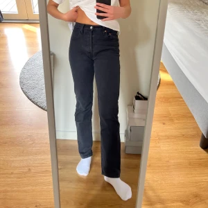 Svarta 501 jeans från Levi's - Snygga svarta jeans från Levi's med klassisk femficksdesign och en bekväm passform. De har en rak passform och är medelhög midja. Storlek 25/30. Det syns att de är använda och de har fått en ljusare färg, men de är hela och fina. Lite stretch också, så de är bekväma.   Knäppning med knappar. 