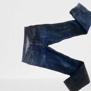 NUDIE JEANS  - Snygga mörkblå jeansbyxor med klassisk femficksdesign och orange sömmar. Perfekta för en avslappnad stil Storlek 32 men passar 30