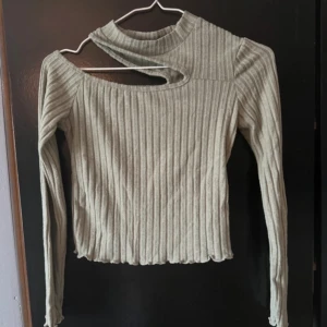 Beige ribbad tröja med asymmetrisk hals - Snygg beige ribbad tröja med en unik asymmetrisk halsdesign. Tröjan har långa ärmar och en modern look som passar perfekt för höst och vår. Perfekt för dig som vill sticka ut med stil!
