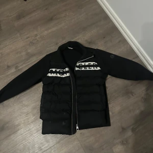Svart kardigan moncler  - Kardigan från moncler en varm modell en fläck nere i vänstra hörnet går förmodligen bort men har inte försökt går it att skanna mobilen mot loggan efter den hamnat i vatten men qr koden funkar bra