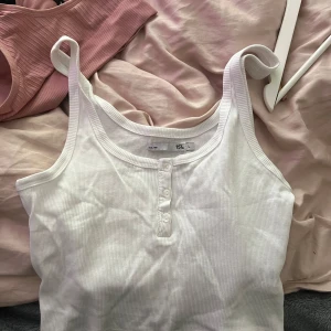 Vit ribbad linnetopp - Säljer en vit ribbad linnetopp med knappar framtill. Perfekt för varma dagar eller som ett basplagg i garderoben. Enkel och stilren design.