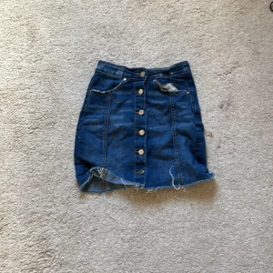 Jeanskjol med knappar - Snygg jeanskjol i blå denim med knappar framtill. 