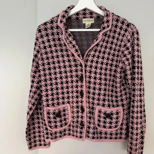 Rosa och svart kofta från Laura Petites - Snygg kofta från Laura Petites i rosa och svart med klassiskt hundtandsmönster. Koftan har långa ärmar, knappar framtill och två fickor med knappdetalj. Materialet är mjukt och stickat, perfekt för dig som gillar retrovibbar och vill sticka ut.