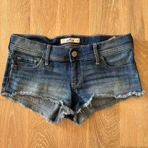 Hollister vintage - Snygga blå jeansshorts från Hollister med fransiga kanter och klassisk femficksdesign. Shortsen har låg midja och slitna detaljer för en avslappnad vibe. Perfekta för sommardagar och festivaler. Materialet är klassisk denim med lite stretch.