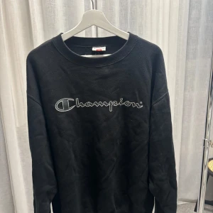 Vintage Champion sweatshirt - Svart sweatshirt från Champion med stor broderad logga över bröstet. Klassisk rund halsringning och långa ärmar. Mjuk bomullskänsla och relaxed fit.