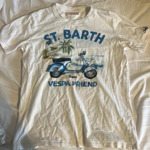 Vit t-shirt MC2 Saint Barth Vespa - Vit t-shirt från MC2 Saint Barth med tryck av blå Vespa, palmer och texten 'ST. BARTH VESPA FRIEND' i blått. Klassisk rund hals och korta ärmar. Perfekt för dig som gillar chill sommarvibbar och snygga prints. Storleken e 12 år och passar nån mellan 150-160 men kan passa större till o med 165 men är lite kort då nypris var runt 700 och köptes förra våren och säljer för mindre en det såklart skriv om ni undrar nåt mvh Arvid