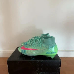 Nike Mercurial fotbollsskor turkos/rosa - Nike Mercurial fotbollsskor i en fräsch turkos färg med neonrosa detaljer och stora loggor. Skorna har snörning, hög strumpkrage och mönstrad ovandel i syntetmaterial. Perfekta för dig som vill sticka ut på planen med stil. Ända defekten är fläcken på bild 4 men annars helt felfria! 