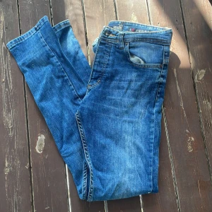 Blå slim fit jeans från Armani - Snygga blå jeans från Armani Jeans i modellen slim fit. Klassisk femficksdesign, läderpatch med logga bak och orange kontrastsömmar. Jeansen är i denim med en schysst tvätt och passar perfekt till en streetig eller clean look.