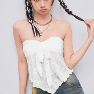 Vit cider tubtopp med knyt - Supersöt vit bandeau tubtopp med knyt framtill och lätt volangig nederkant. Toppen är ärmlös och har ett diskret blommigt mönster i tyget. Perfekt till jeans eller kjol för en fräsch look. Tunn och luftig, passar perfekt till varma dagar.