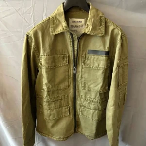 Olivgrön field jacka Zadig & Voltaire - Säljer en olivgrön utilityjacka från Zadig & Voltaire med flera fickor framtill, dragkedja och klassisk krage. Jackan har en cool militärinspirerad look och är tillverkad i bomull. Perfekt för dig som gillar streetstyle och praktiska detaljer.