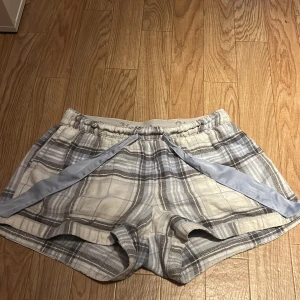Rutiga shorts från Hollister XS - Supermysiga rutiga shorts från Hollister i grått, vitt och ljusblått. De har elastisk midja med logga och en ljusblå snörning framtill. Perfekta för chill dagar eller som pyjamasshorts. Mjukt bomullsmaterial och klassisk loose fit.