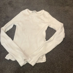 Vit ribbad långärmad tröja - Säljer en vit långärmad tröja från C i storlek 146/152. Tröjan är ribbad och har en enkel, clean look med rund hals. Perfekt att styla med jeans eller kjol för en chill och snygg outfit.