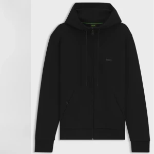 Svart hoodie från BOSS med dragkedja - Svart hoodie från BOSS med diskret logga på bröstet, hel dragkedja och huva med snörning. Tröjan har långa ärmar, ribbade muddar och två fickor framtill. Tillverkad i mjuk bomullsblandning för en skön och avslappnad stil.