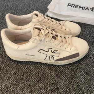 Premiata vita sneakers  - Snygga vita sneakers från Premiata i med grå detaljer och logga på sidan. Klassisk rund tå, snörning och coolt mönstrad sula. Perfekta för dig som gillar stilrena och trendiga skor. Skorna kommer med originalpåse. Väldigt sparsamt använda och i toppskick! Mitt pris är 1699👍 Vid frågor/liknande är det bara att höra av sig!