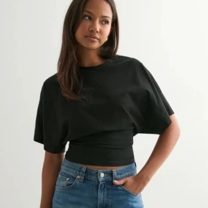 Svart croppad topp med loose fit - Svart croppad topp med bred resår i midjan och loose fit över axlarna. T-shirten har rund halsringning och korta, vida ärmar.