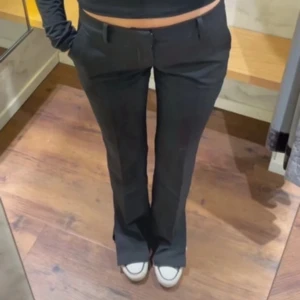 Svarta bootcut kostymbyxor - Snygga svarta kostymbyxor med bootcut passform och hällor för bälte. Byxorna har klassisk design med raka ben som blir vidare nedtill. Perfekta för en clean och stilren look. Materialet känns mjukt och följsamt. Ej min första bild! Säljer då de är förstora! Slitsen längst ner är ihopsydd men går lätt att sprätta upp om så önskas.