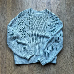 Ljusblå stickad tröja från Pieces - Superfin ljusblå stickad tröja från Pieces med coola hålmönstrade ärmar och ribbade muddar. Tröjan har en relaxed fit och är perfekt för dig som gillar en mysig men ändå trendig look. Passar perfekt till jeans eller kjol!