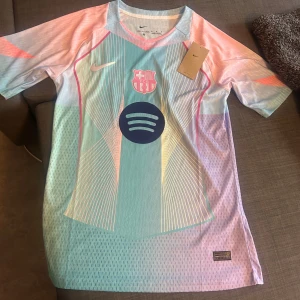 Barça x Nike pastell fotbollströja - Säljer en FC Barcelona fotbollströja från Nike med Spotify-logga. Tröjan har korta ärmar och är gjord i ett lätt, ventilerande material. Färgerna är pastellblå, rosa, lila och orange med vita och rosa detaljer samt grafiskt mönster. Perfekt för dig som vill sticka ut. Använd en gång! Storlek M men kan även passa som S lite oversized.