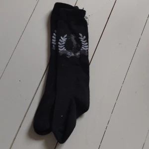 Svarta ridstrumpor med hästmotiv - Svarta ridstrumpor med ett snyggt grått hästmotiv omringat av stiliserade grå lagerblad upptill.