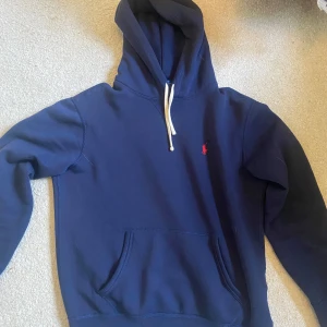 Marinblå hoodie från Polo Ralph Lauren - Säljer en marinblå hoodie från Polo Ralph Lauren. Jag är 180 cm lång och den passar precis. Jag har bara haft den i någon månad.