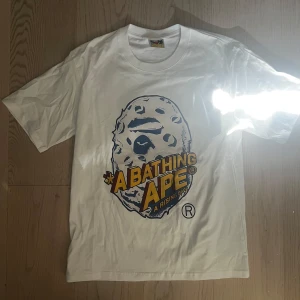 Vit BAPE t-shirt med tryck, S - Vit t-shirt från BAPE med stort grafiskt tryck på både fram- och baksidan. Klassisk rund hals och korta ärmar. Materialet är mjuk bomull och det finns en liten BAPE-tag på nederkanten. Snygg streetwear med färgglada detaljer i gult och blått.