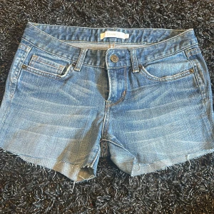 Blå jeansshorts med rå kant från Cue - Snygga blå jeansshorts från Cue med klassisk femficksdesign och rå, fransig kant nertill. Shortsen har ljusa slitningar framtill och bakfickor med dekorativ söm. Perfekta för varma dagar och enkel att matcha med allt.