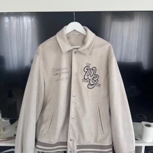 Beige bomberjacka från Zara XL - Snygg beige Varsity jacka från Zara i storlek XL. Jackan har broderade detaljer med text och stjärnor på bröstet, ribbade muddar och knäppning med tryckknappar. Materialet känns mjukt och mockaliknande, självklart är det faux suede.