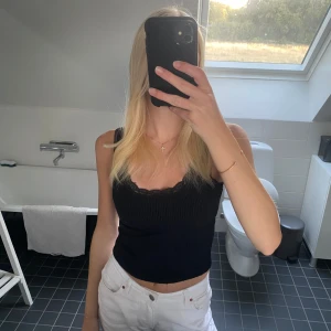 Svart ribbad linnetopp med spets - Säljer en svart ribbad linnetopp med smala axelband och snygg spetskant vid urringningen. 