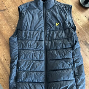 väst från Lyle & Scott - Snygg mörkblå dunväst från Lyle & Scott med gul logga på bröstet. Västen har inga defekter och är i toppskick. Passar både S/M super!
