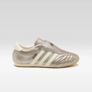 Adidas Taekwondo sneakers  - Säljer ett par Adidas taekwondo sneakers i metallic guldaktigt och creme-vitt med klassiska tre ränder på sidan. Skorna är stilrena men tuffa, rund tå och platt sula. Perfekt för dig som gillar retro och sportig stil.!! Slip-in modell. Dem är endast använda en gång.