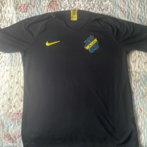 AIK svart fotbollströja Nike M - AIK fotbollströja i svart från Nike med gul logga och klubbmärke på bröstet. Tillverkad i lätt och ventilerande VaporKnit-material som passar perfekt för träning eller match. Klassisk rund hals och korta ärmar. Snygg och stilren design för dig som älskar AIK.