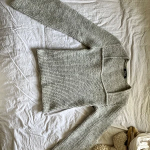 Grå stickad tröja med trumpetärmar - Supermysig ljusgrå stickad tröja från Gina med ribbad struktur och trumpetärmar. Tröjan har en fyrkantig ringning som ger en snygg och modern look. Använd ca 2 gånger, jättefint skick och passar perfekt till ett par svarta jeans 