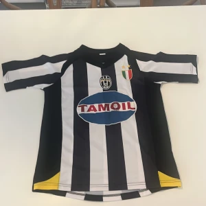 Juventus Del Piero 10 matchtröja - Juventus fotbollströja med Del Piero och nummer 10 på ryggen. Klassisk svartvit randig design, Tamoil sponsor på bröstet och klubbmärke med två stjärnor. Kortärmad modell i lätt och ventilerande material, inslag av gult vid sidorna. Perfekt för fans av italiensk fotboll.