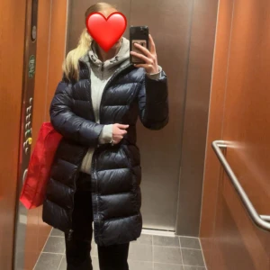 COLMAR jacka - Säljer en lång, mörkblå dunjacka från Colmar med huva och dragkedja hela vägen. Jackan är lång till mitten av låren (kanske lite längre) är 166cm lång. Ena fickan är sönder och har en liten liten lagning på ena armen som knappt syns. Orginal pris 6000kr, kan diskutera pris