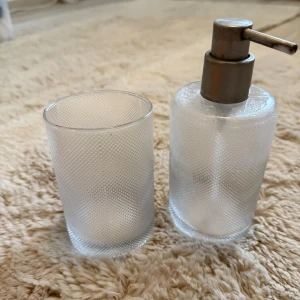 Glas frostat set - Två stilrena behållare i frostat glas, en med pump i metall och en öppen kopp. Perfekt för förvaring i badrum/kök.