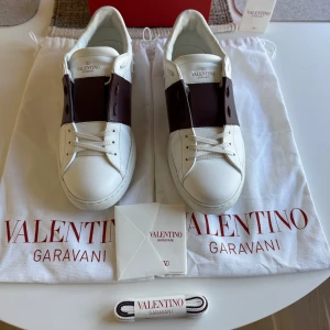 Valentino Garavani Open sneakers vit/vinröd - Säljer mina Valentino Garavani skor i jättebra skick. Färgen är Burgundy (brun) och är eftertraktad. Box, snören och äkthetsbevis medföljer vid köp! Hör av dig för fler bilder!