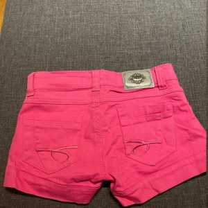 lowwaisted shorts - Snygga rosa jeansshorts från Issue de Look med klassiska fem fickor, dekorativa knappar vid benslut och cool detalj med metallmärke bak. Perfekta för varma dagar och ger en färgstark vibe till din outfit. dragkedjan är trasig 