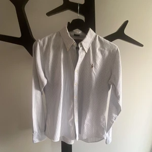 Ralph Lauren Skjorta - Snygg blårandig skjorta från Ralph Lauren i slim fit-modell. Skjortan har klassisk krage, knappar framtill och det ikoniska broderade polospelaren på bröstet. Tillverkad i 100% bomull för en skön och fräsch känsla. Perfekt för dig som gillar stilrena och tidlösa plagg.