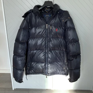Ralph lauren jacka  - Snygg svart pufferjacka från Polo Ralph Lauren med huva och dragkedjor. Köpt för ungefär 6-7 tusen i vintras, den har använts väldigt lite så den är fortfarande i väldigt bra skick! För mer frågar skriv privat!