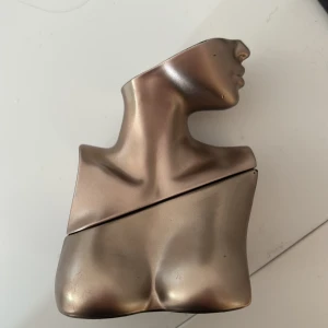 Parfymflaska i bronsformad torso - Unik parfymflaska formad som en stiliserad kvinnlig torso i metallisk bronsfärg. Flaskan har mjuka, skulpterade linjer och en modern design som sticker ut på hyllan. Perfekt för dig som gillar konstnärliga detaljer och snygga accessoarer. Billie eilish parfym lite mindre än hälften kvar 
