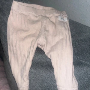 Ljusrosa ribbade leggings Newbie baby 1-3mån  - Säljer ett par ljusrosa leggings från Newbie med ribbad struktur. De har elastisk midja och är gjorda i mjukt bomullsmaterial, perfekta för chill dagar. Passar dig som gillar enkel och clean stil.