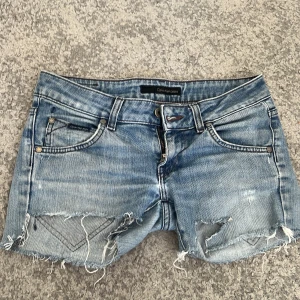 Blå jeansshorts från Calvin Klein - Snygga blå jeansshorts från Calvin Klein med slitna detaljer och råa kanter. Klassisk femficksmodell med låg midja och coola sömmar på bakfickorna. Perfekta för sommardagar när du vill ha en avslappnad och trendig look.