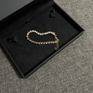Guldigt armband med glittriga stenar - Snyggt armband i guldton med stora, glittrande stenar som ger en lyxig känsla. Länken är justerbar med en kedja för perfekt passform. Perfekt accessoar för att lyfta din stil och dra blickarna till sig. Helt nya oanvända Vid retur står köparen för Frakten/Returen. Jag ansvarar inte för postens slarv.