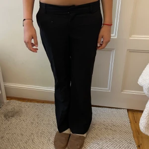 Svarta kostymbyxor med raka ben - Säljer ett par svarta kostymbyxor med klassisk rak passform och midja med hällor för bälte. Byxorna har diskreta bakfickor och är perfekta för en clean och stilren look. Materialet känns mjukt och följsamt.