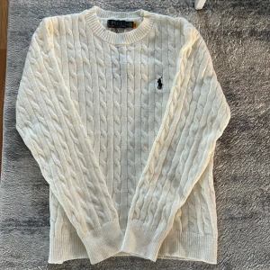 Vit kabelstickad tröja Polo Ralph Lauren - Säljer en vit kabelstickad tröja från Polo Ralph Lauren i storlek M. Tröjan har rund hals, långärmade ribbade muddar och den klassiska broderade loggan på bröstet. Perfekt för dig som gillar clean och stilren look.