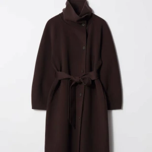 & Other Stories brun Ullkappa - Säljer en lång, mörkbrun kappa med oversized passform och hög krage. Kappan har knappar framtill och ett matchande bälte i midjan för snygg siluett. Tillverkad i ullblandning, perfekt för kyliga dagar. Långa ärmar och stilren design som ger en clean look. Den är använd endast en gång så den är som ny. Nypris 2990kr