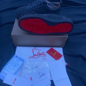 Christian Louboutin svarta sneakers mocka - Svarta sneakers från Christian Louboutin i mocka med ikonisk röd sula och nitar på tån. Skorna har snörning och en stilren, rund tå. Perfekta för dig som vill sticka ut med exklusiva detaljer och lyxig känsla. 4 hörn i box av  har fixat boxen dock prutat å klar 1150kr ej lägre 