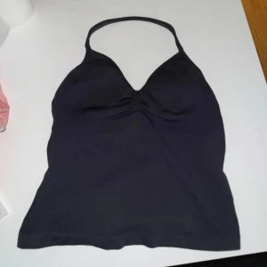 Svart halterneck linne - Snyggt svart linne med halterneck och lätt rynk vid bysten. Toppen är ärmlös och har en smickrande v-ringning. perfekt till gym