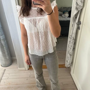 Vit spetsblus med volangärm från Nelly - Supersöt vit blus i spets från Nelly med rund hals. Blusen är transparent, har fina spetsdetaljer och knytning i nacken. Storlek S. 