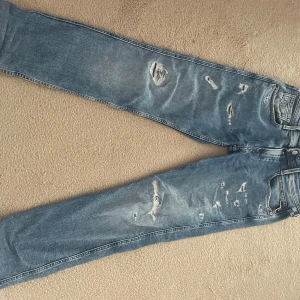 Ljusblåa replay Anbass med slitningar - Säljer ett par blå jeansbyxor från Replay med slitna detaljer och raka ben. Jeansen har klassisk femficksdesign och normal passform. Perfekta för en avslappnad och trendig look. Jeansen är helt i nyskick inköpta för cirka 1300 och jag säljer för 699. Storleken är 28/30.